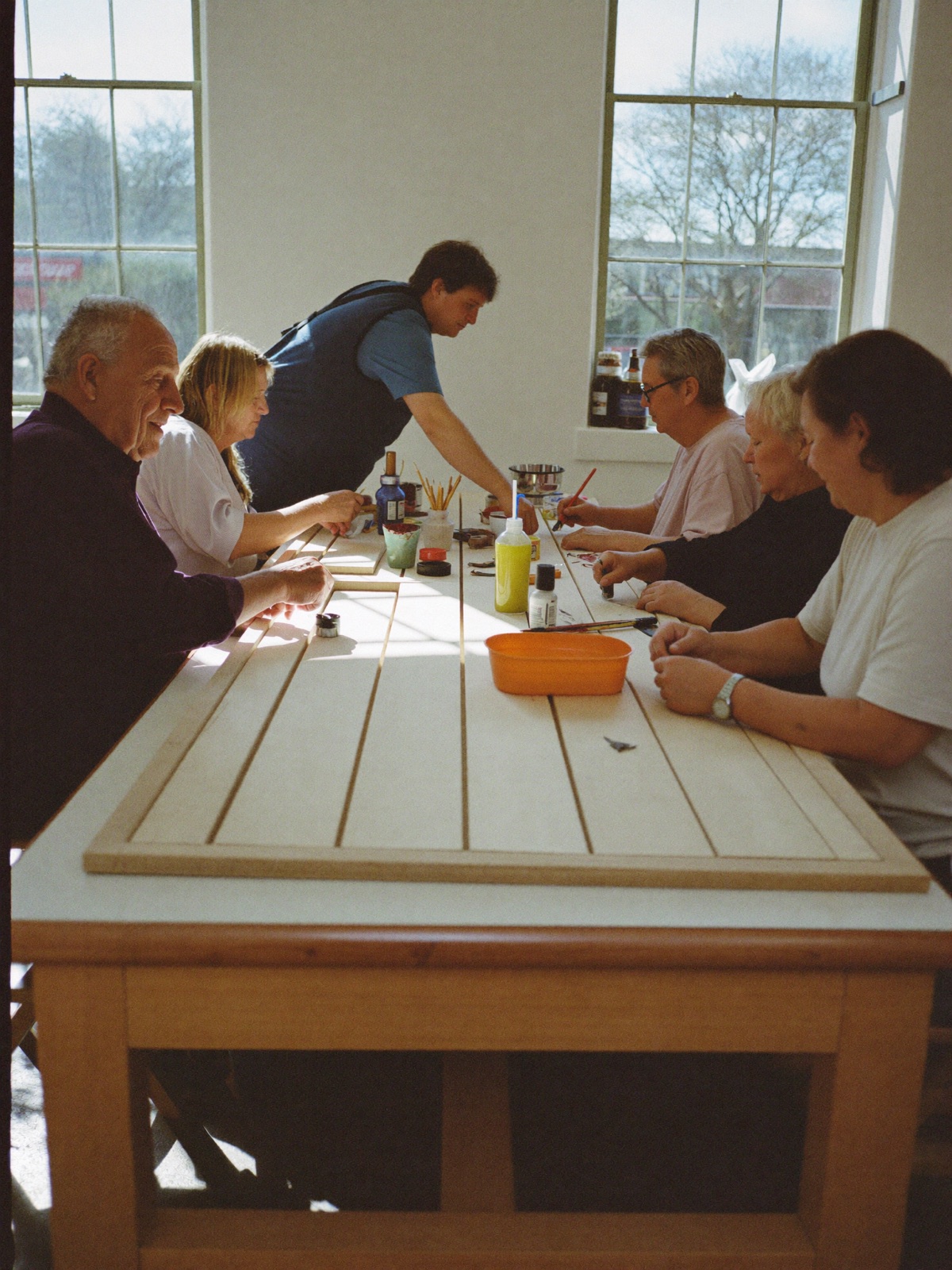 Deelnemers werken aan een lange tafel in een lichte werkplaats